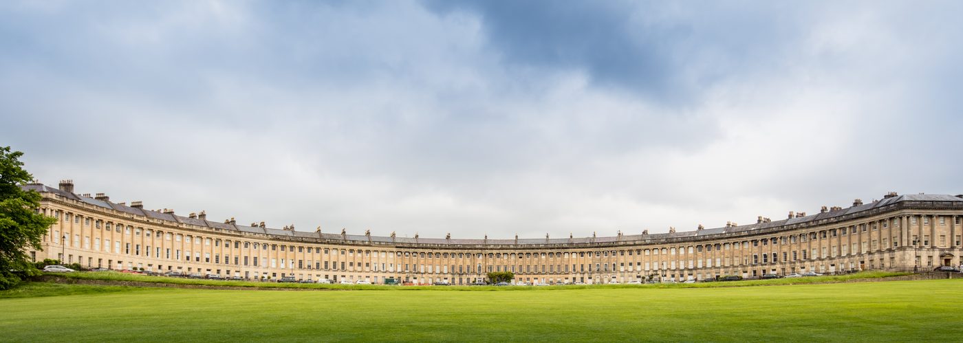The long curve of a Georgian crescent in Bath seen across a lawn, built of honey-coloured stone